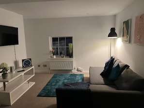 A living room with a sofa, a TV, a radiator, a window, and a lamp. - Apartment Sleeps 4 Street Parking Were Available (Brighton)