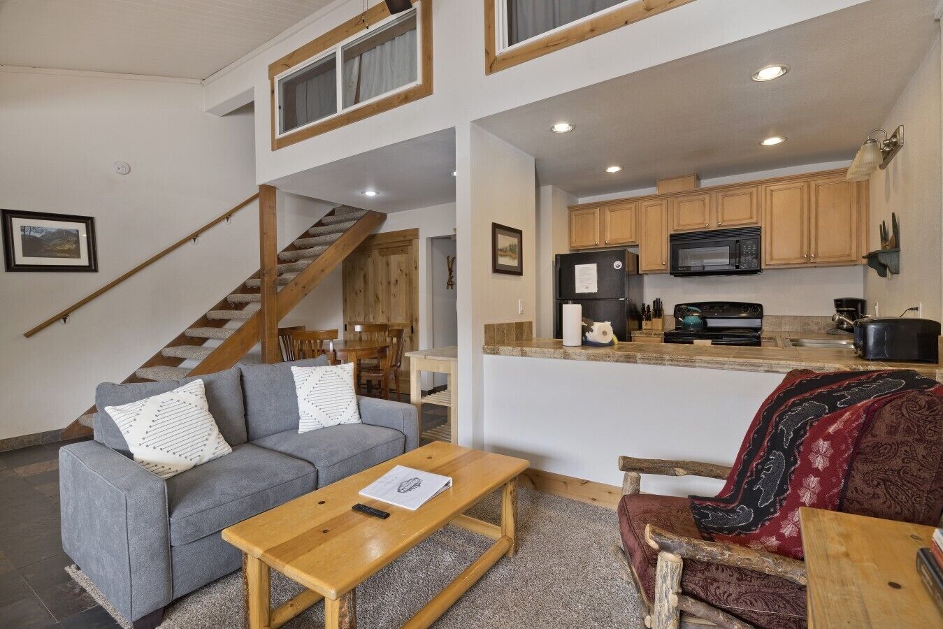 A modern interior with a grey sofa, wooden coffee table, and a red sofa with a patterned throw. A staircase leads to an upper level.