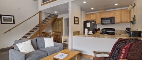 A modern interior with a grey sofa, wooden coffee table, and a red sofa with a patterned throw. A staircase leads to an upper level.