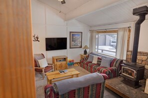 A cozy living room with a fireplace, a television, a sofa, and a window with a view. - Sierra Manors Mountain Escape (Mammoth Lakes)