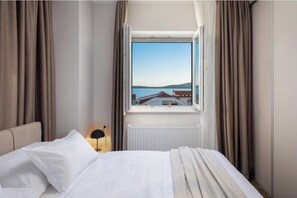 Ein Hotelzimmer mit Bett, einem Vorhangfenster, einer Lampe und Blick auf ein Gebäude gegenüber dem Wasser.
