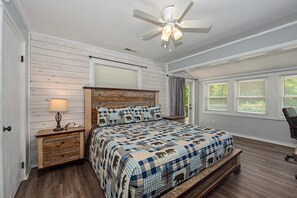 Un dormitorio con cama, cabecera de madera, mesita de noche, lámpara y ventilador de techo.
