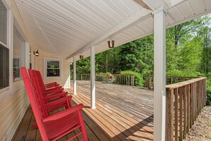 A covered wooden deck with red chairs, white railings, and a view of a forested area. - Baskins Creek 406 (Gatlinburg)