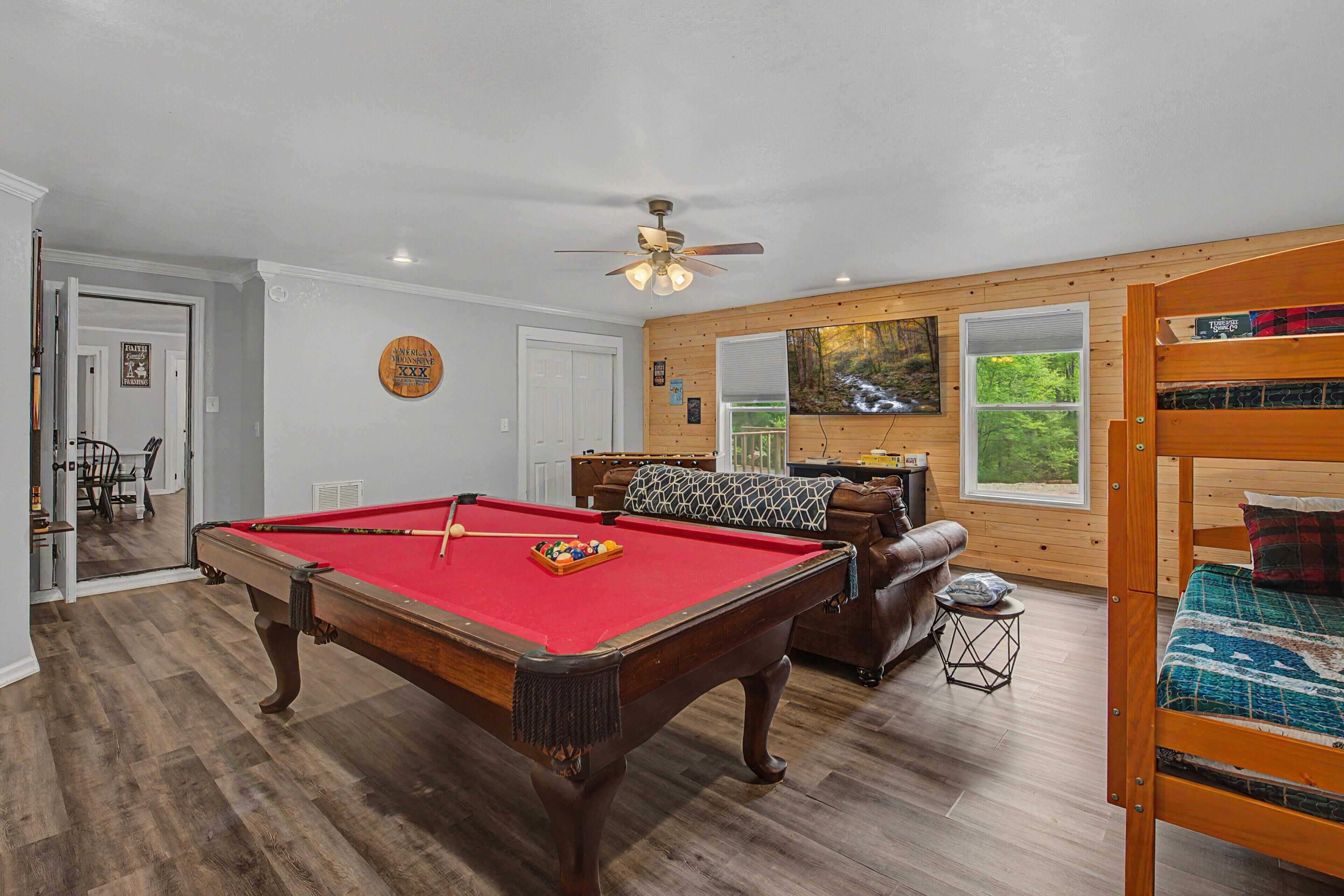 A pool table in a room with wooden walls, a ceiling fan, and a bunk bed.