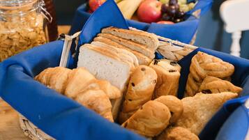 A basket of assorted breads and pastries, a jar of granola, and a bowl of fruit.