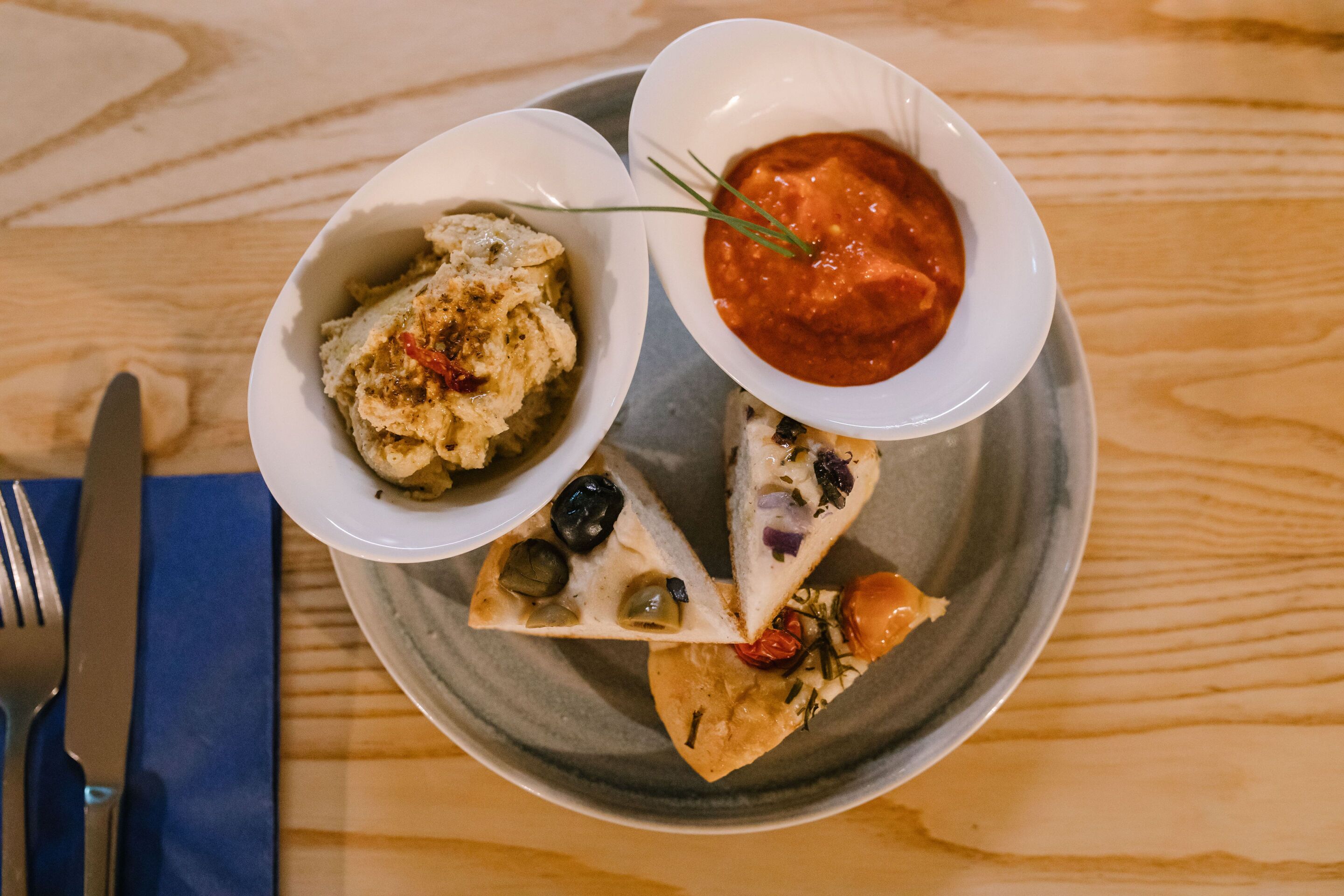 Ein Teller mit verschiedenen Speisen, darunter eine Schüssel Hummus, eine Schüssel rote Soße und eine Pizza mit Oliven und Tomaten.