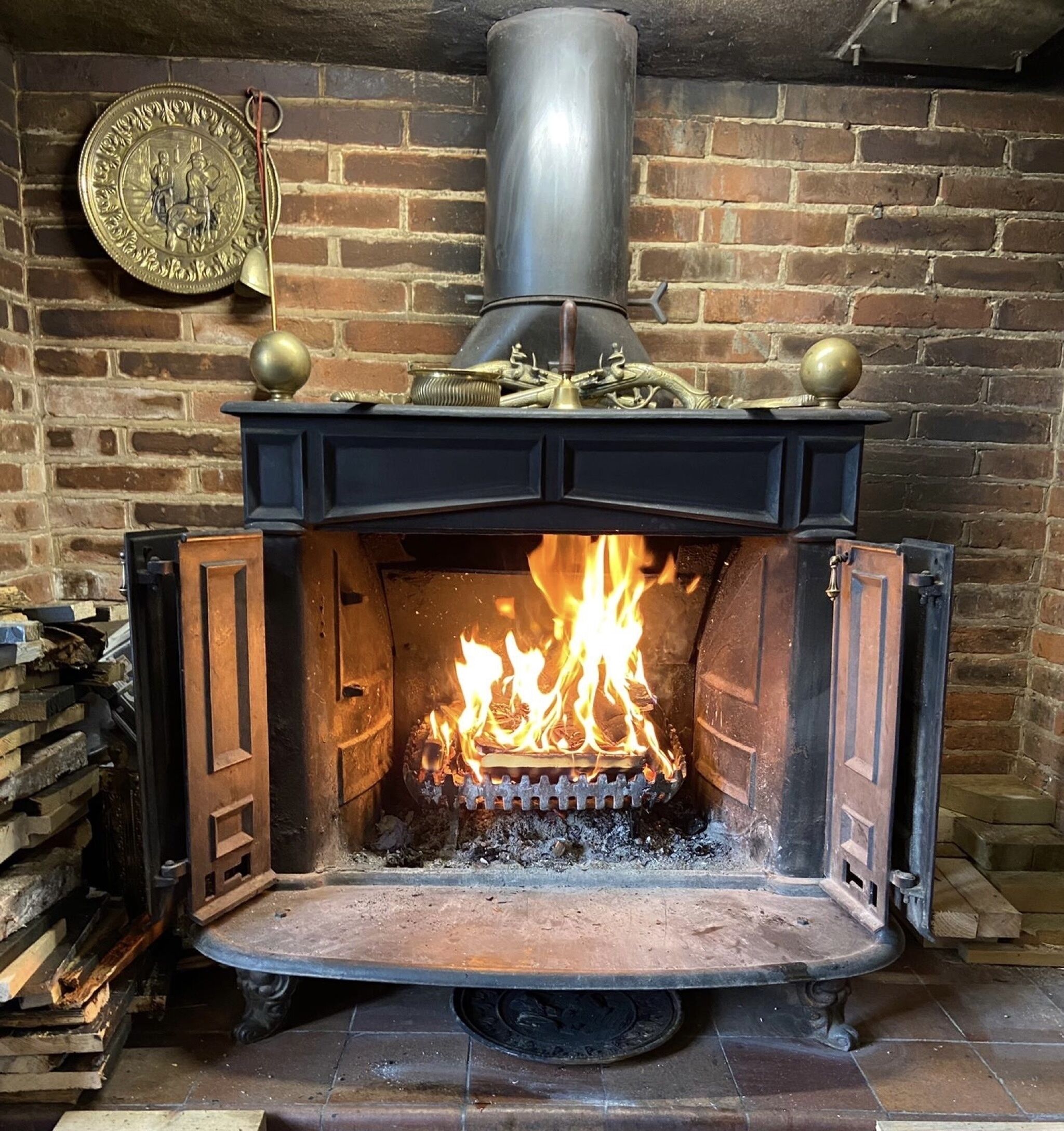 A traditional fireplace with a fire burning inside, a metal chimney, and a decorative plate on the wall.