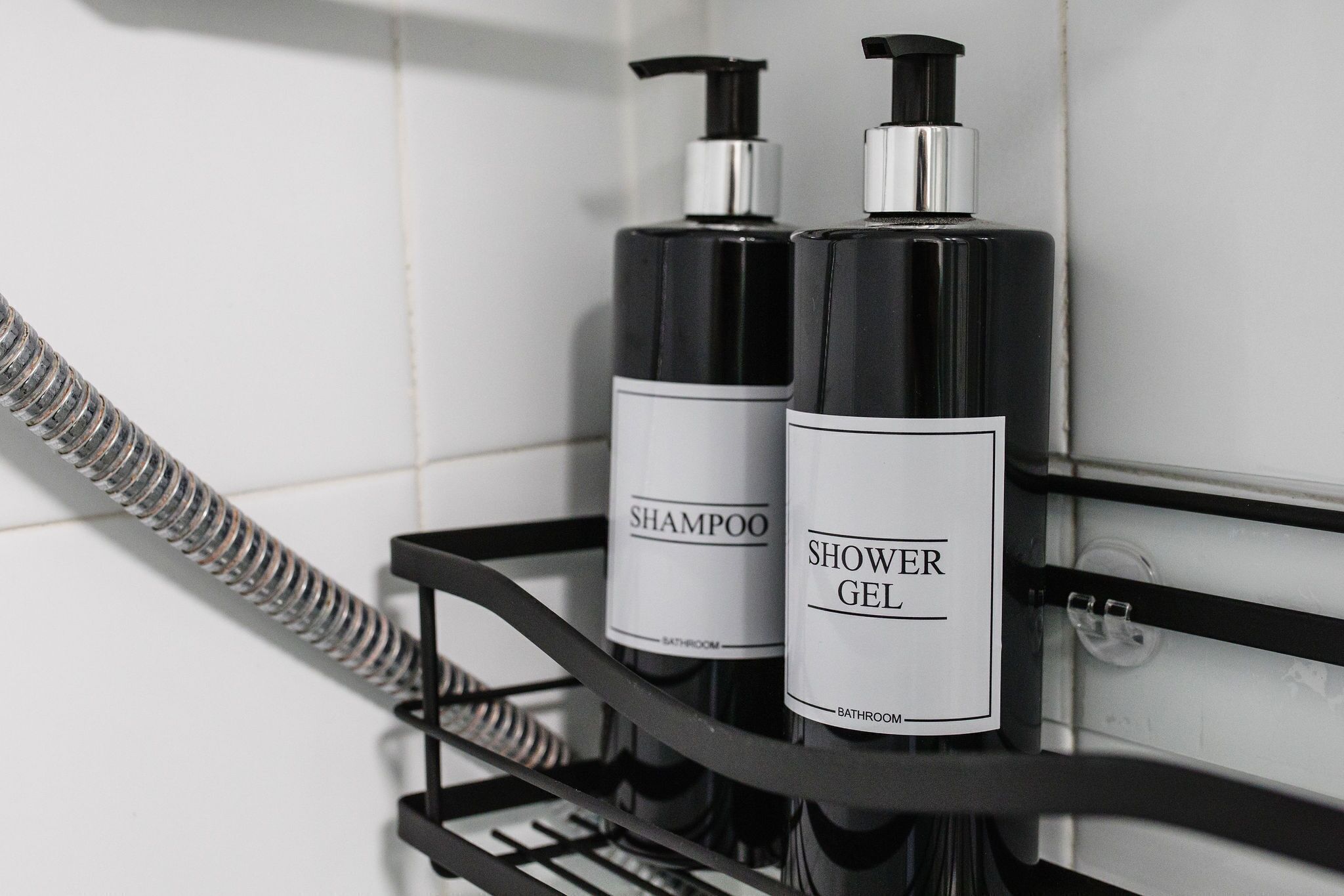 Two bottles of shampoo and shower gel on a black metal rack in a bathroom.