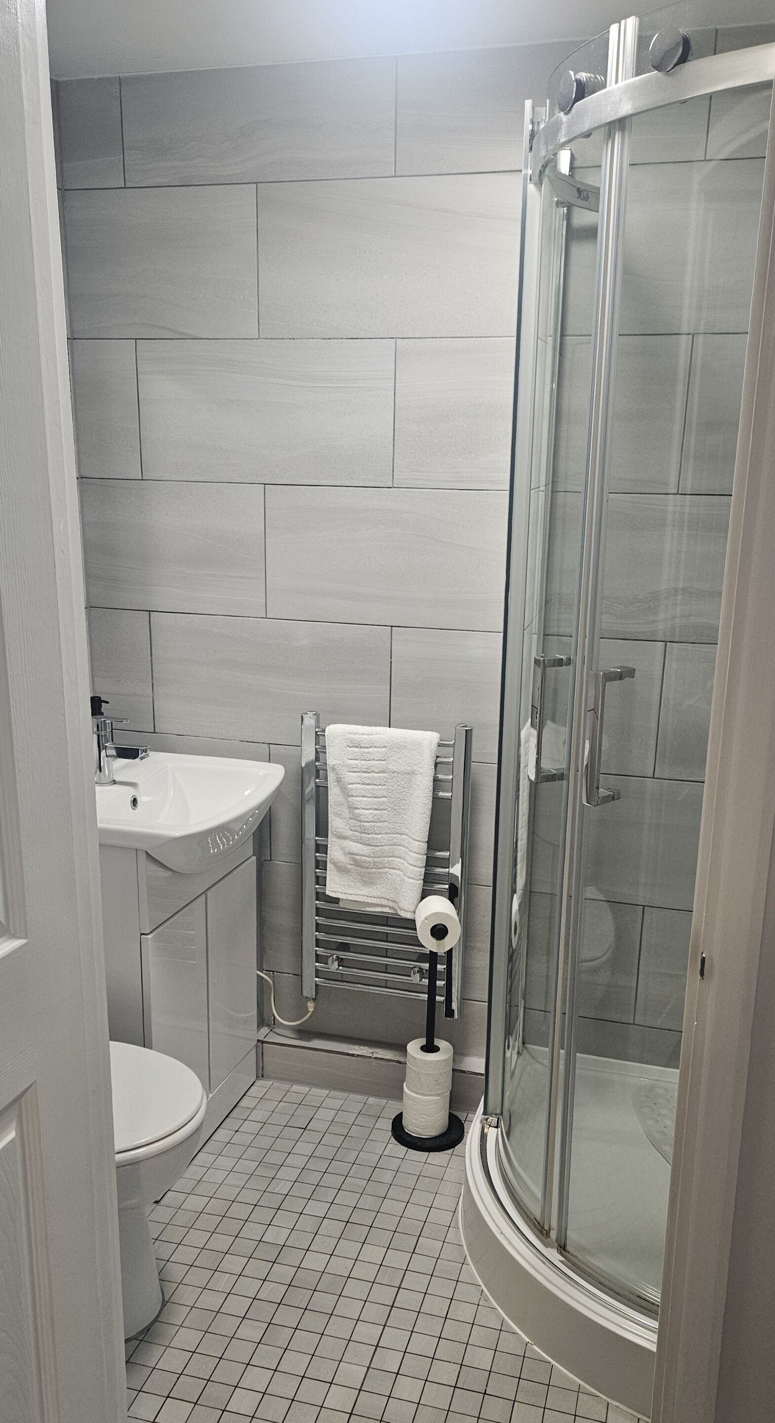 A bathroom with a shower, toilet, sink, and towel rack.