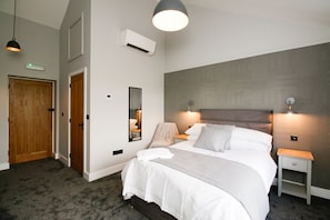 A bedroom with a large bed, bedside lamps, an air conditioning unit, a wooden door, and a mirror. - The Kings Arms Broad Green (Broad Green)