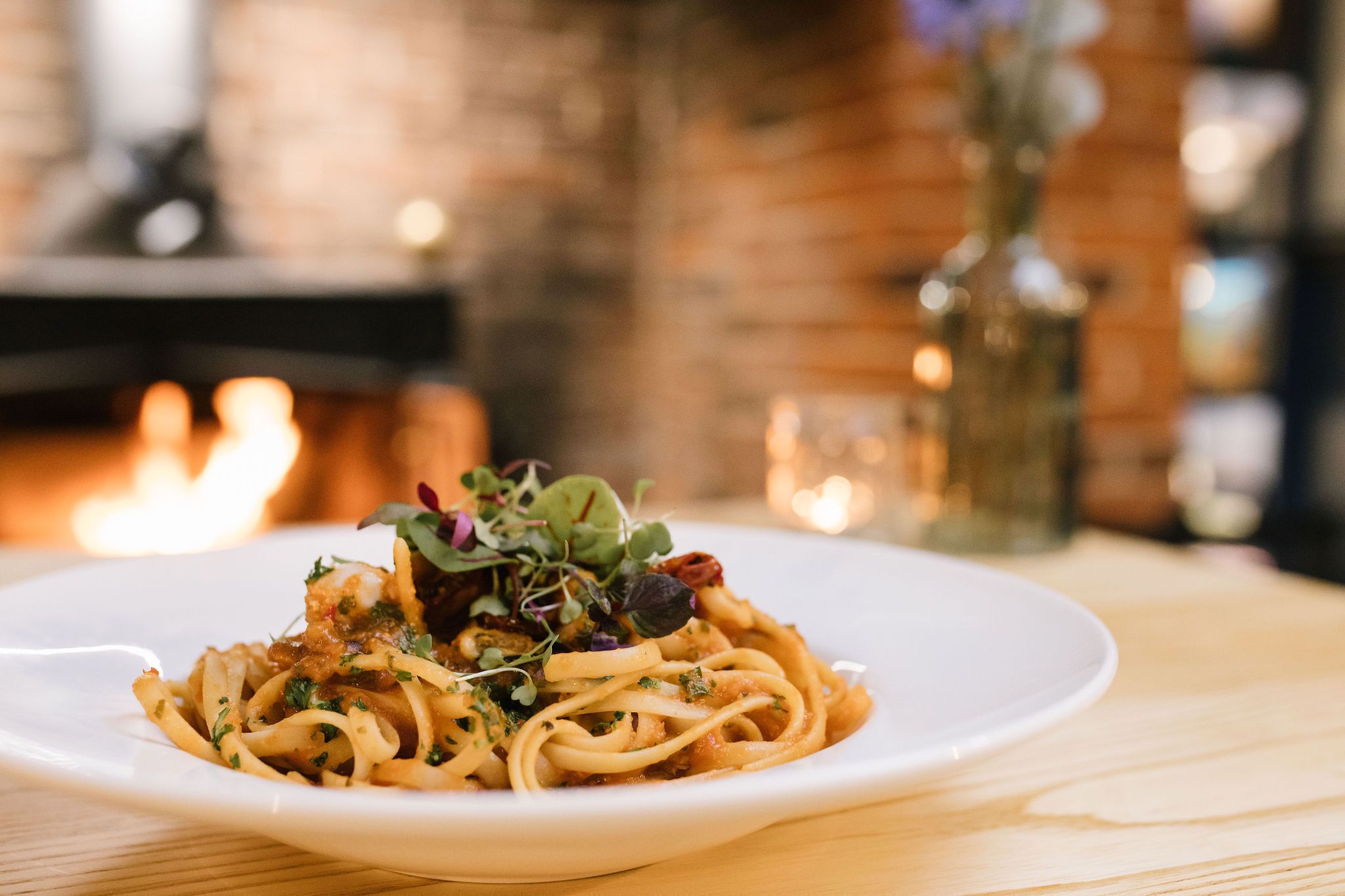 A plate of pasta with greens and a candle in the background.