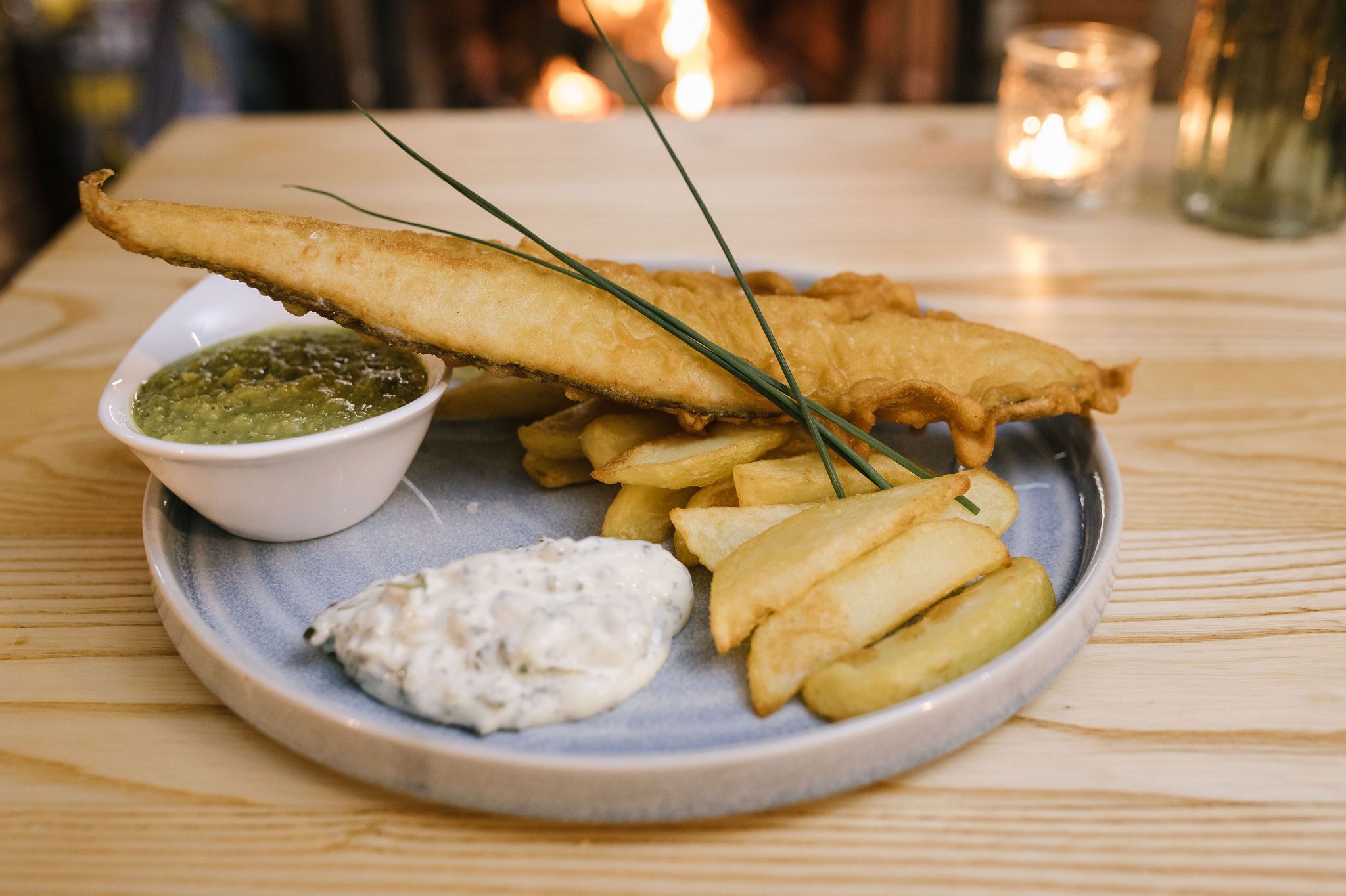 Een bord vis en friet met twee dipsauzen en een kaarsje op de achtergrond.
