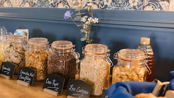 A display of various food items in glass jars with labels, set against a patterned wall.