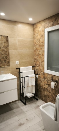 A bathroom with a stone wall, a white sink, a black towel rack with towels, and a toilet.. Golden Sky Big Families