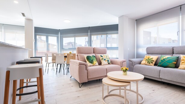 Una sala moderna con un sofá, dos mesas redondas y una zona de comedor con sillas.