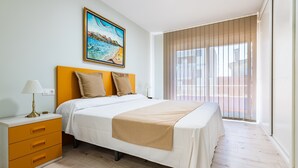 Un dormitorio con cama, mesita de noche, lámpara, cuadro y vistas al exterior.