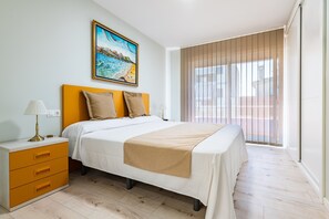 Un dormitorio con cama, mesita de noche, lámpara, cuadro y vistas al exterior.
