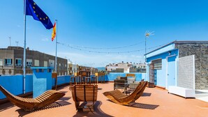 Una terraza en la azotea con sillones de descanso, una bandera y un muro de piedra.