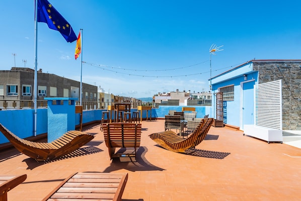 A rooftop terrace with lounge chairs, a flag, and a stone wall.