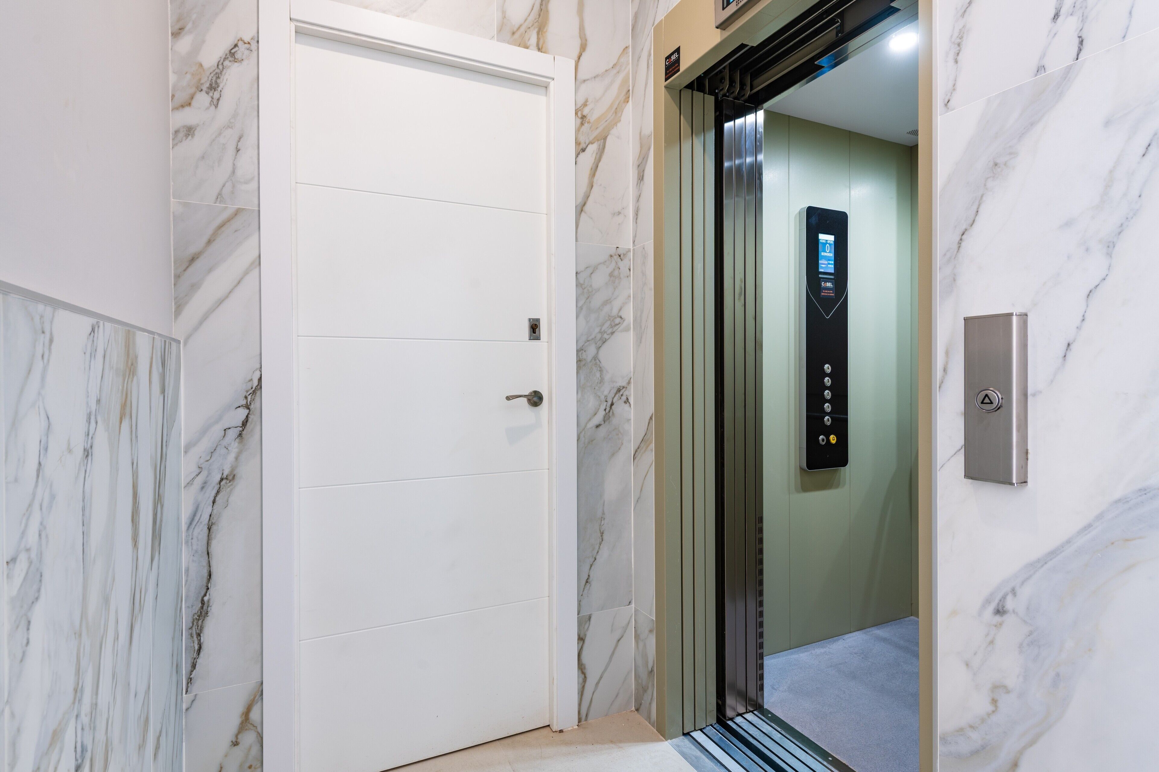 An elevator with a control panel, a white door, and marble walls.
