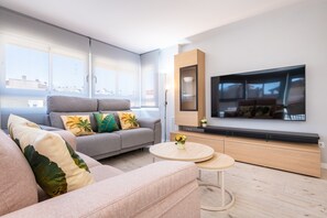 Un salon moderne avec un canapé gris, une table basse ronde en bois et un téléviseur à écran plat fixé au mur.
