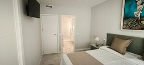 A bedroom with a bed, a nightstand, a lamp, a painting, and a door leading to another room. - Apartment 'Golden Sky 3ª' with Shared Terrace, Wi-Fi and Air Conditioning (Benicarló)