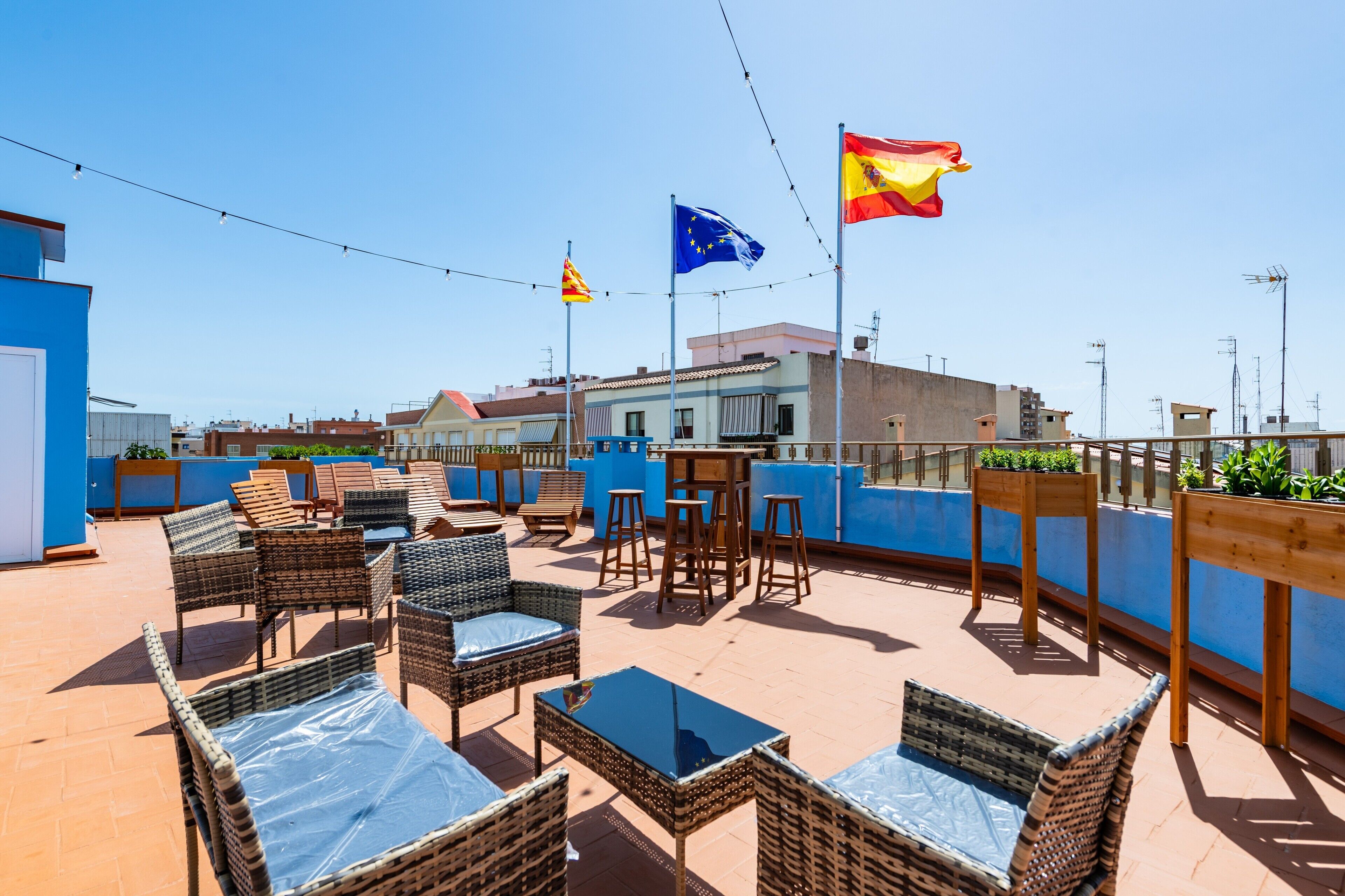 Terraza en la azotea con mobiliario de mimbre, una mesa y banderas.