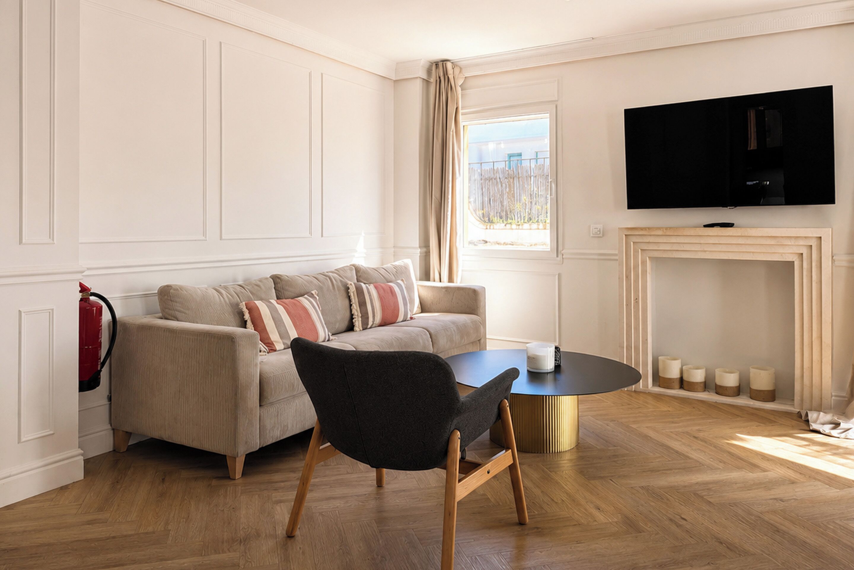 A living room with a sofa, a black chair, a coffee table, a fireplace, and a TV mounted on the wall.