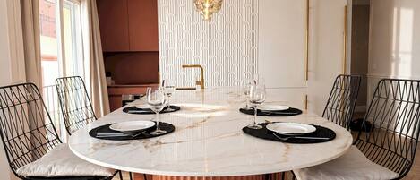 Un espace repas avec une table ronde en marbre, des chaises en fil de fer noir et un lustre doré.