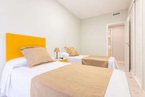 Une chambre d’hôtel avec deux lits, un mur d’accent jaune vif et une porte blanche.