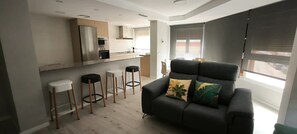 A modern kitchen with a built-in oven and microwave, a grey sofa with cushions, and a bar stool area. - Apartment 'Golden Sky 2ª' with Shared Terrace, Wi-Fi and Air Conditioning (Benicarló)