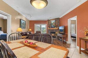 A dining area with a wooden table set for four, a fireplace, and a living room with a sofa and television. - Baskins Creek 409 (Gatlinburg)