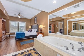 Ein Schlafzimmer mit Bett, Nachttischlampen, einem großen Spiegel und einem Badezimmer mit Badewanne und Waschbecken.