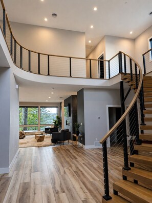 Un intérieur spacieux agrémenté d’un escalier en colimaçon, de parquets en bois et de grandes fenêtres offrant une vue sur la verdure.