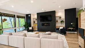 A modern living room with a large sectional sofa, a fireplace, and a television. - Modern Deep Creek Lakefront Home, Movie Theater, Hot Tub, 7BR/6BA, Sleeps 16 (Oakland)