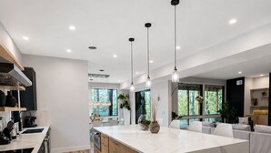 A modern kitchen with a large island, wooden flooring, and pendant lighting. - Modern Deep Creek Lakefront Home, Movie Theater, Hot Tub, 7BR/6BA, Sleeps 16 (Oakland)