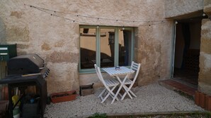 A patio with a grill, a table and chairs, and a window with string lights. - Charming 3 Bed/2 Bath House in Medieval Village (Tillac)