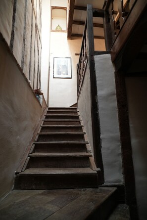 Un escalier en bois, doté d’une rampe, mène à une pièce où un tableau encadré est accroché au mur.