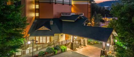 A multi-story building with a sloped roof, a staircase leading to the entrance, and a well-lit driveway.