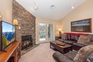 A living room with a stone wall, a fireplace, a leather sofa, a coffee table, and a television. - Baskins Creek 504 (Gatlinburg)