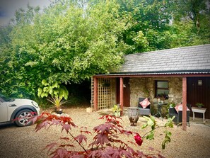 A stone building with a tiled roof, a gravel driveway, and a car parked in front. - Cozy Cottage Retreat in Donegal (Ballintra)