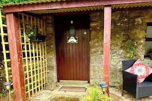 A stone building with a wooden door, a wooden fence, and a chair outside.