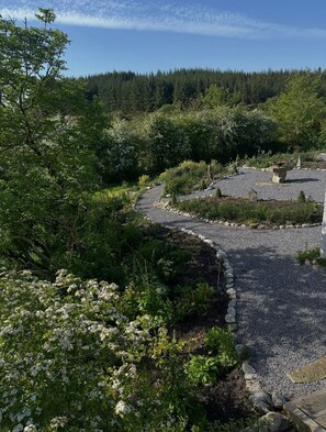 A garden with a gravel path, surrounded by greenery and a forest in the background. - Cottage - Sleeps 3 - Parking - Garden - Lake Side (Ballintra)