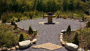 Un jardín con una estructura de piedra central, rodeado de grava y diversas plantas.