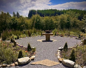 A garden with a central stone structure, surrounded by gravel and various plants.