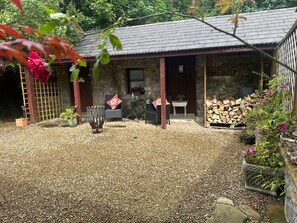 A stone building with a tiled roof, a gravel driveway, outdoor seating, and a pile of firewood. - Cozy Cottage Retreat in Donegal (Ballintra)