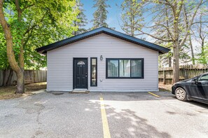 Un petit bâtiment d’un seul étage, avec une porte et des fenêtres noires, une allée en gravier et une voiture garée.