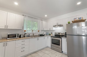 Una cocina moderna con armarios blancos, electrodomésticos de acero inoxidable, microondas, tostadora y refrigerador.