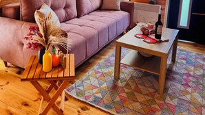 Um quarto aconchegante com teto inclinado, um sofá estofado, uma pequena mesa com uma garrafa e um tapete colorido.