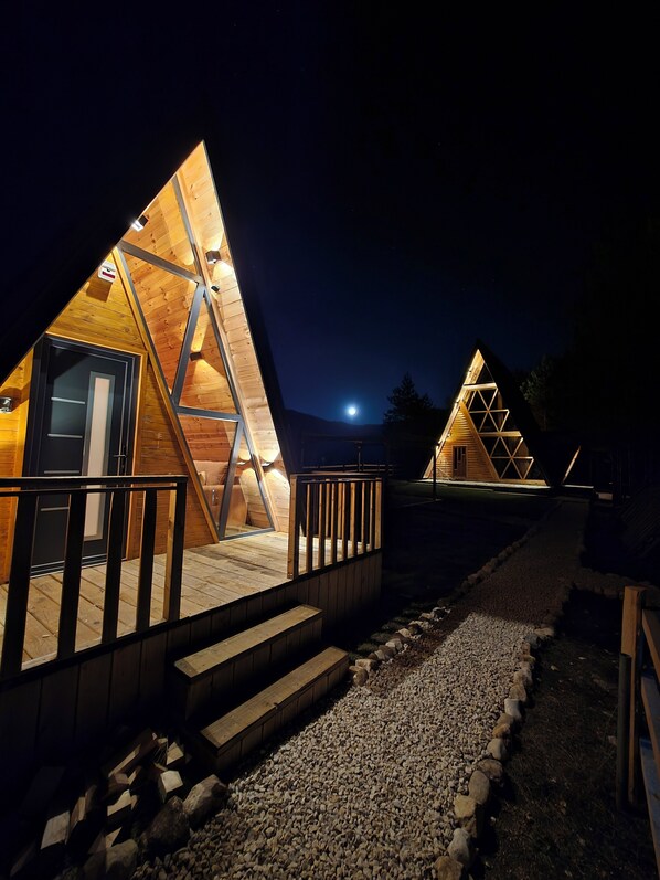 Deux cabanes triangulaires en bois, dotées d’escaliers extérieurs et de rampes de protection en métal.